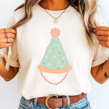 A close-up of a woman wearing a cream t-shirt printed with a light mint green party hat decorated with pastel hearts and stars.