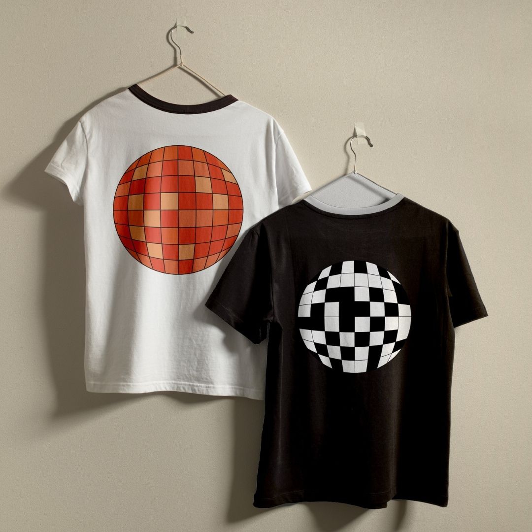 Two short-sleeve ringer t-shirts hanging on hangers against a plain beige wall. The left shirt is white with a dark collar and features a large orange and red checkerboard disco ball graphic on the back.