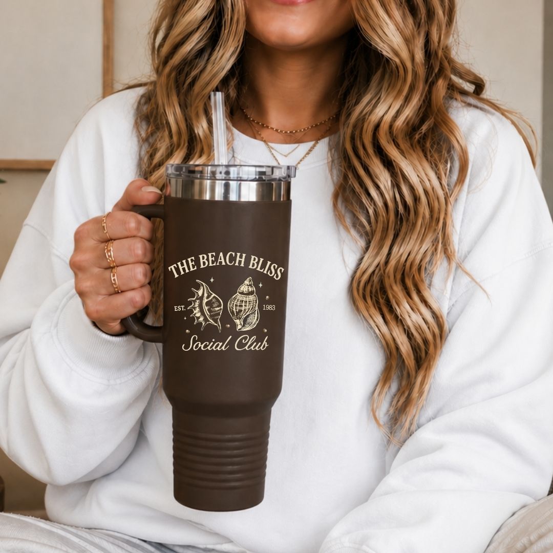 A woman in a white sweatshirt holding a 40oz brown travel tumbler with a handle, featuring a high quality cream sublimation print of a vintage seashell beach club design.