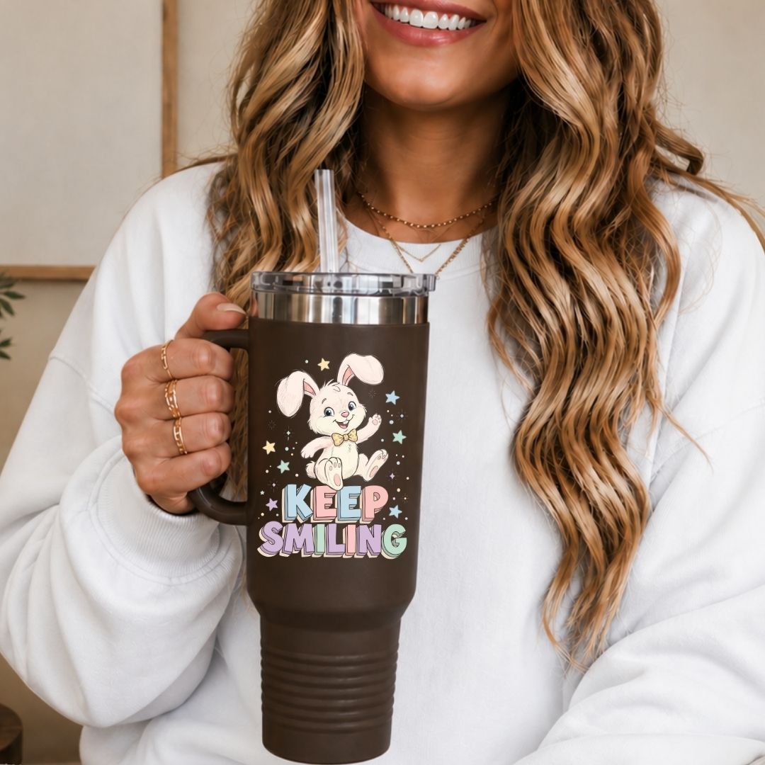 A woman in a white sweatshirt holding a 40oz brown travel tumbler with a handle, featuring a high quality colorful sublimation print of a smiling cartoon bunny.