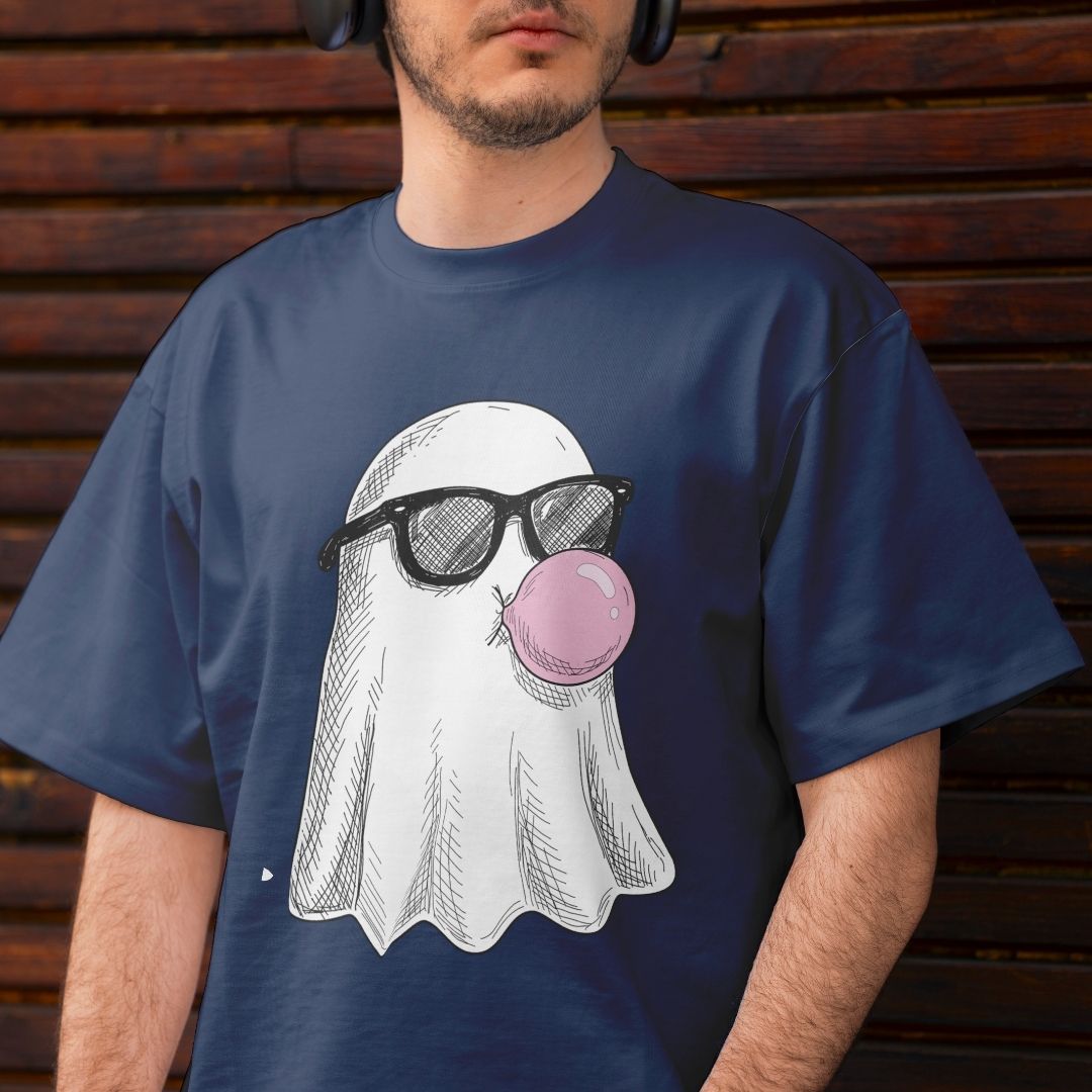 A man wearing a navy blue t-shirt with a graphic of a white ghost wearing black sunglasses and blowing a pink bubblegum bubble, set against a dark wooden background.