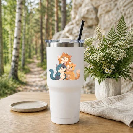 White travel tumbler with a black straw featuring a cute cartoon cats graphic, set outdoors on a wooden table with nature background.