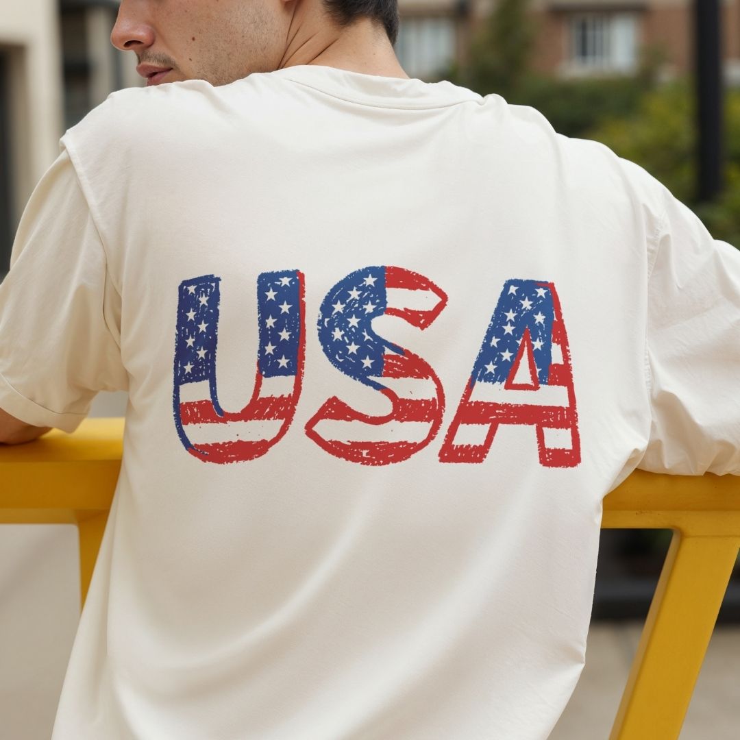 Person wearing a white t-shirt with 'USA' printed on the back, sitting outdoors.