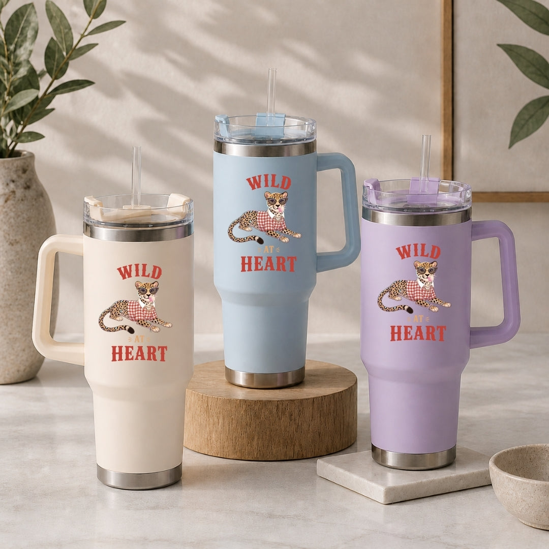 Three insulated tumblers in beige, light blue, and purple, each featuring the fun "Wild At Heart" leopard illustration.