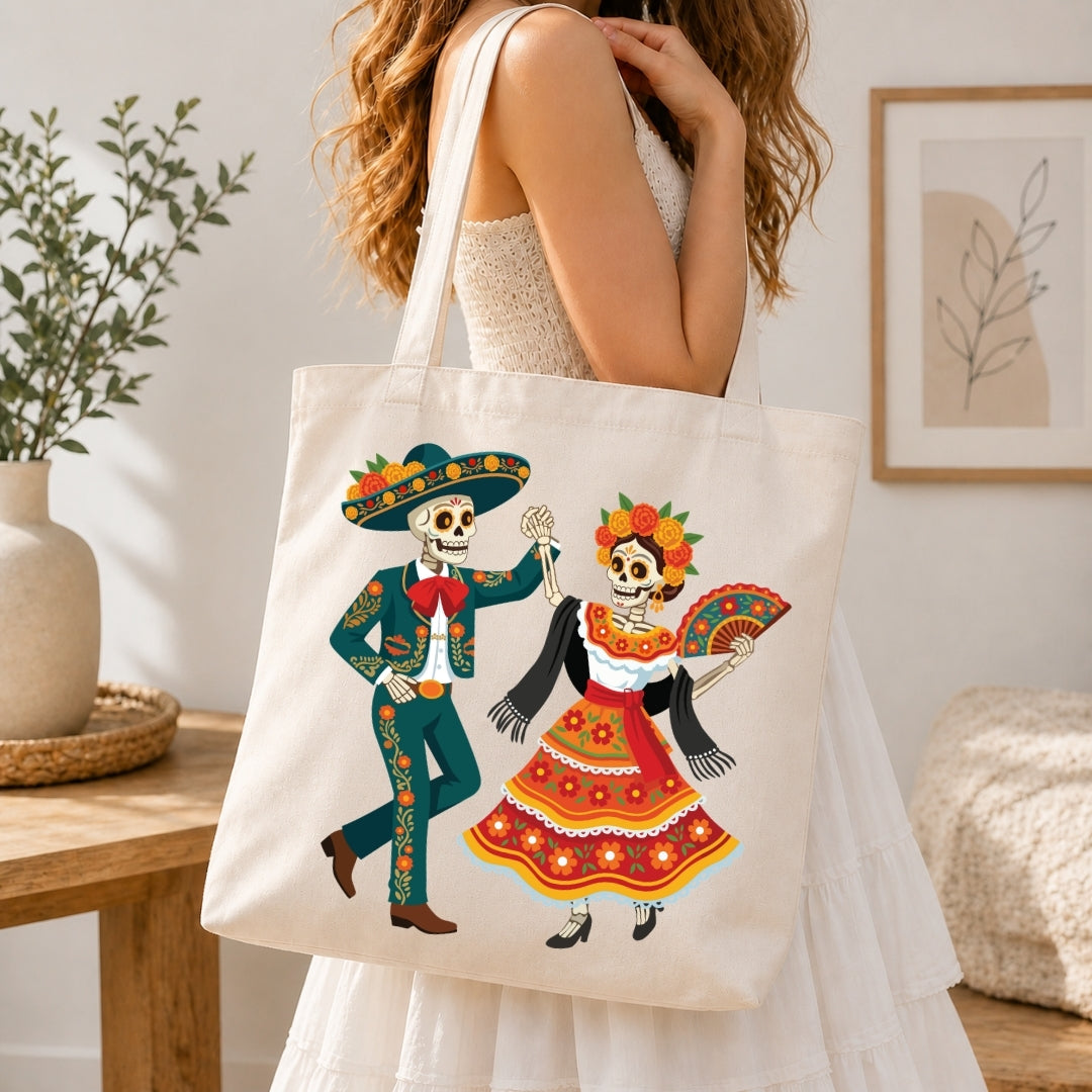 A woman in a white dress carries a cream canvas tote bag featuring a colorful Day of the Dead sugar skull illustration. The scene is set in a bright, modern room with a wooden table, potted plant, and framed wall art.