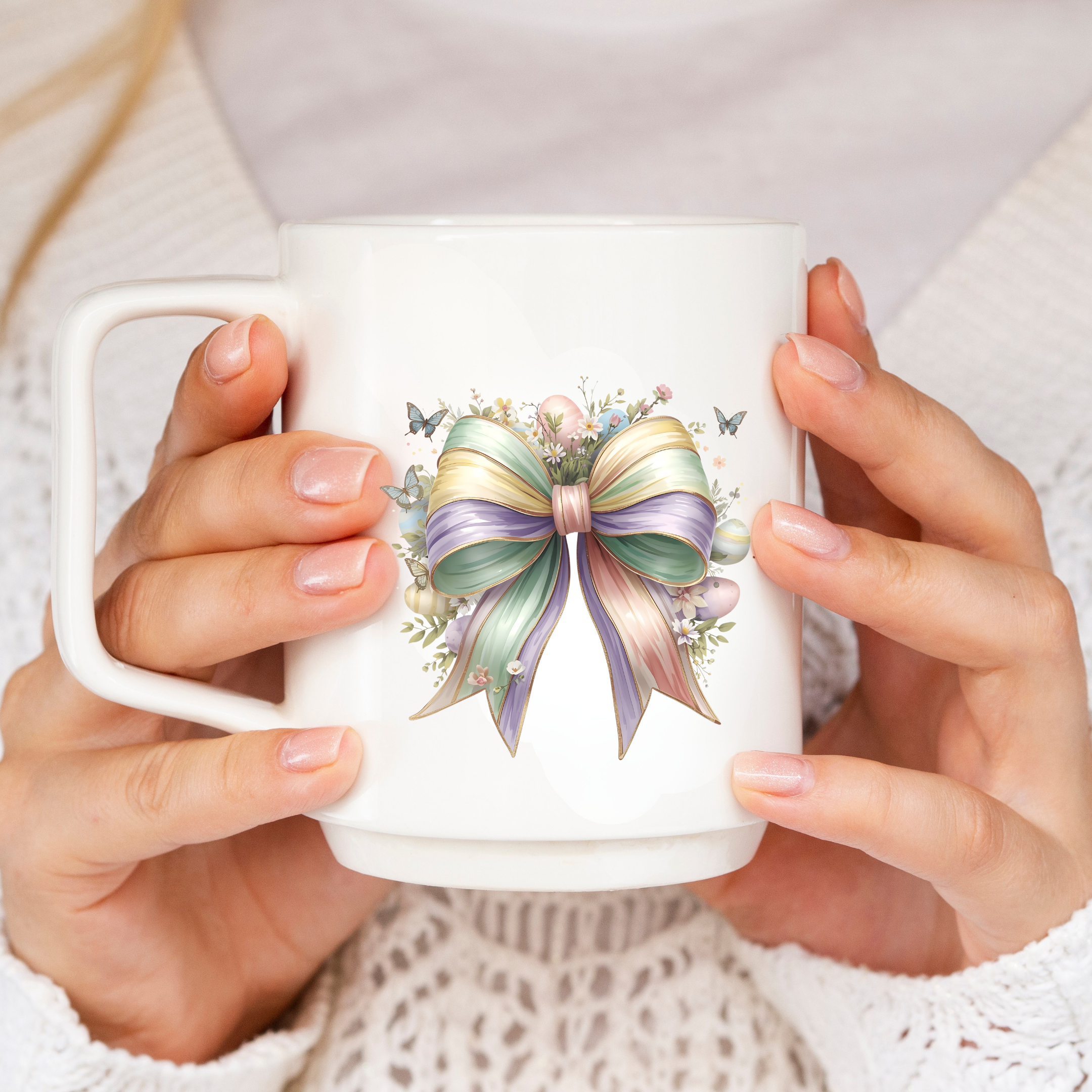 White mug with a colorful bow design held by hands against a neutral background