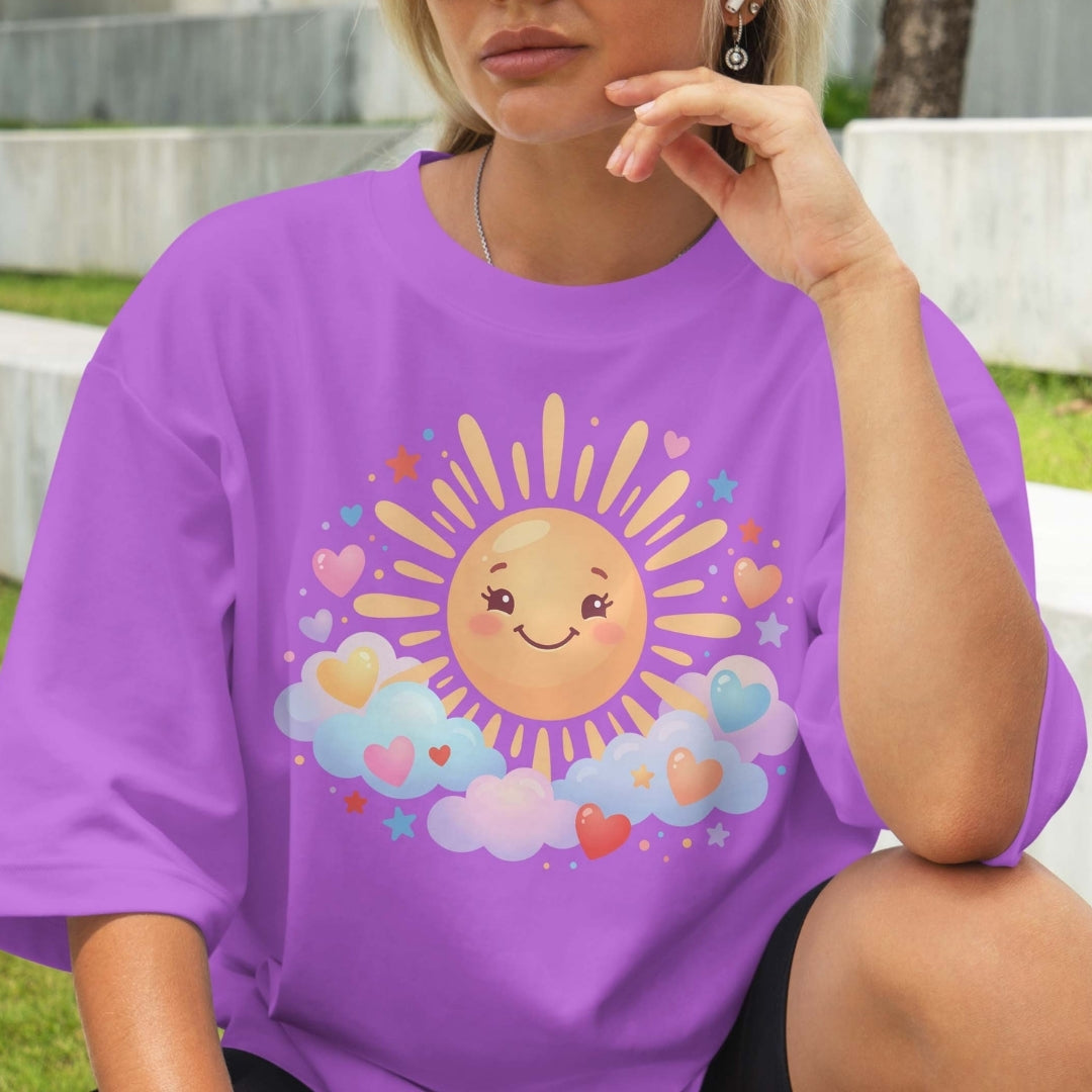 Person wearing a purple t-shirt with a sun and cloud design outdoors.