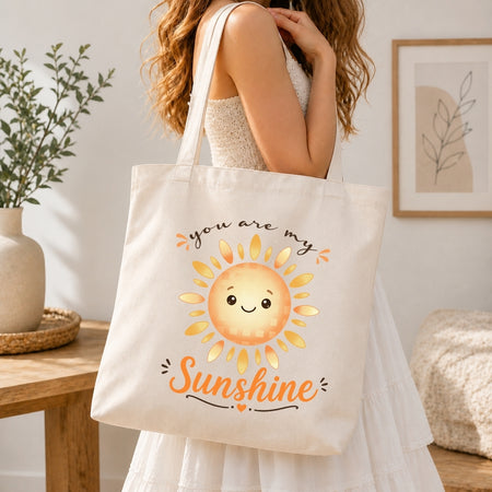 A person holding a cream-colored tote bag printed with the happy cartoon sun graphic and the text "you are my Sunshine".