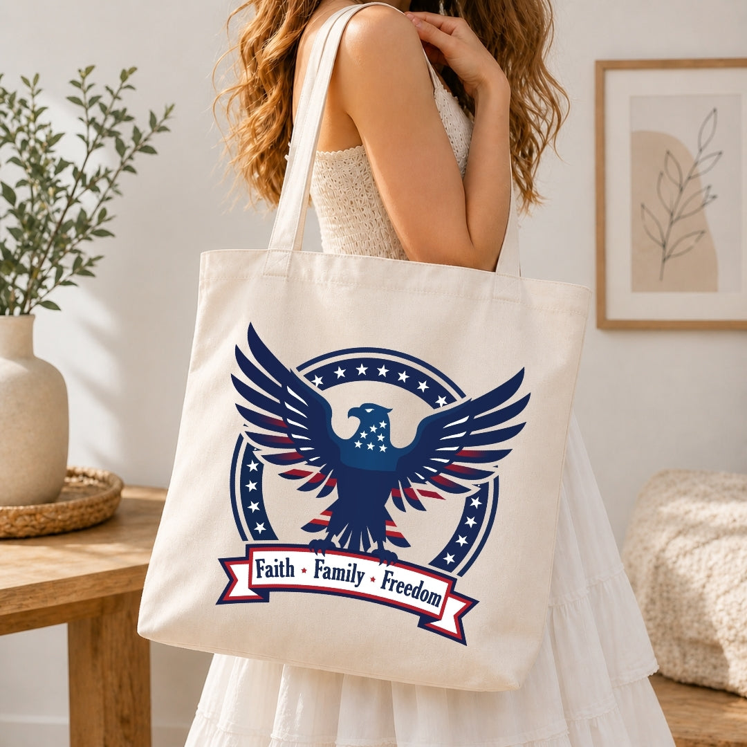 A woman holding a cream-colored tote bag printed with the patriotic eagle graphic and the text "Faith • Family • Freedom".