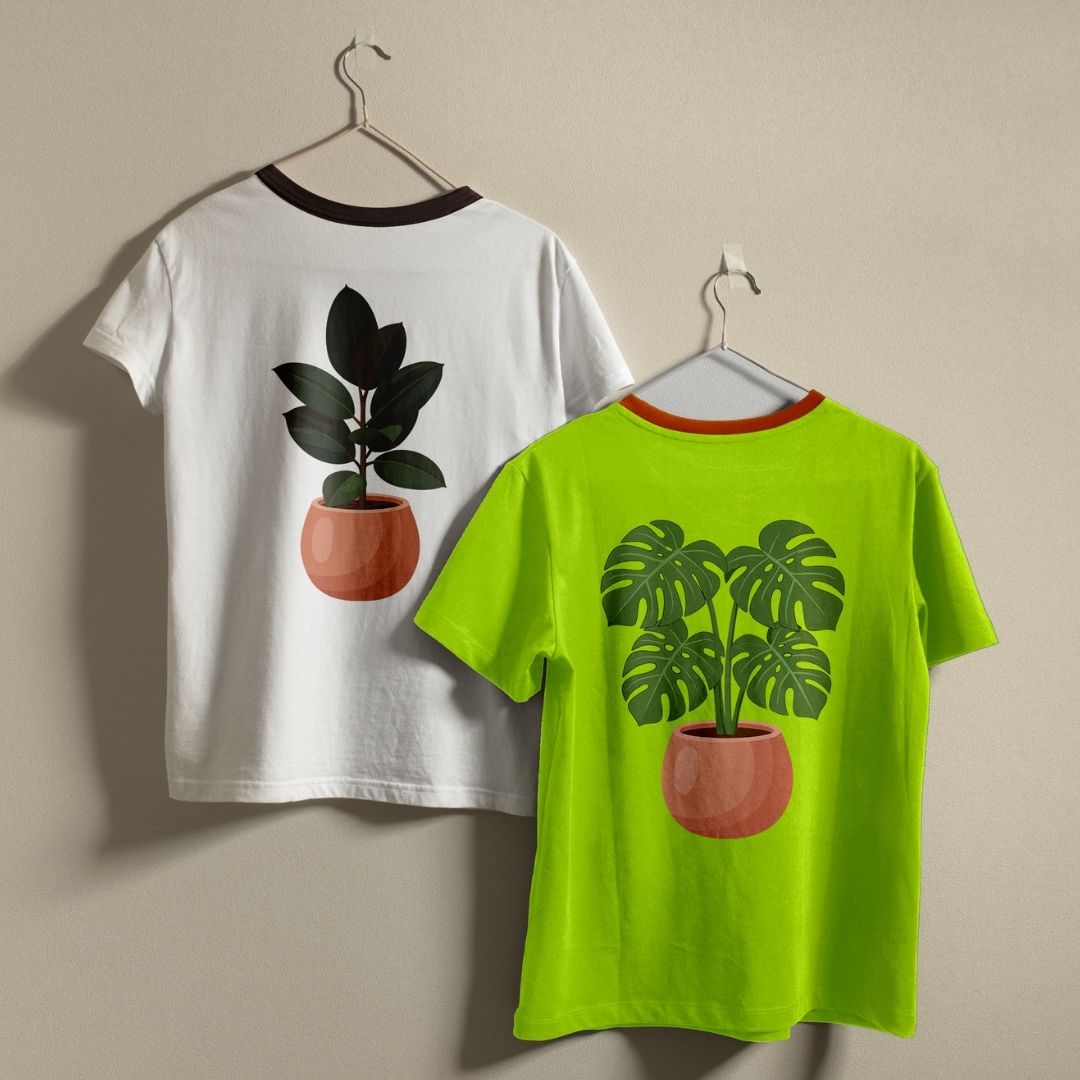 Two ringer t-shirts hanging on metal hangers against a plain beige wall. The left shirt is white with a black collar trim and features a graphic of a potted plant on the back.