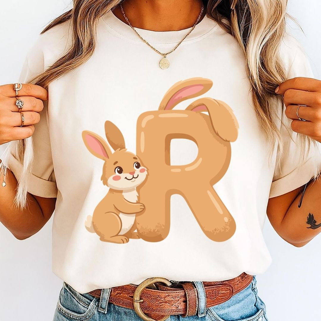 A woman holding the sides of an off-white t-shirt featuring a light brown letter R with bunny ears and a friendly cartoon rabbit hugging it.