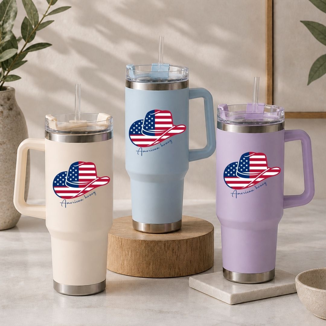 Three insulated travel tumblers in cream, light blue, and lavender purple arranged on a table, all showcasing the patriotic western design.