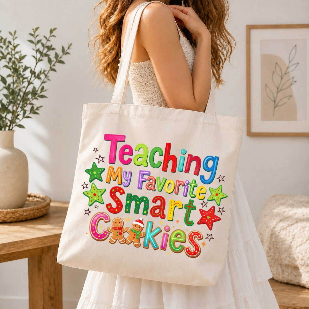 A woman in a white dress carries a cream canvas tote bag with colorful text reading 'Teaching My Favorite Smart Cookies' and decorated stars and cookies. The scene is set in a bright, modern room with a wooden table, potted plant, and framed wall art.