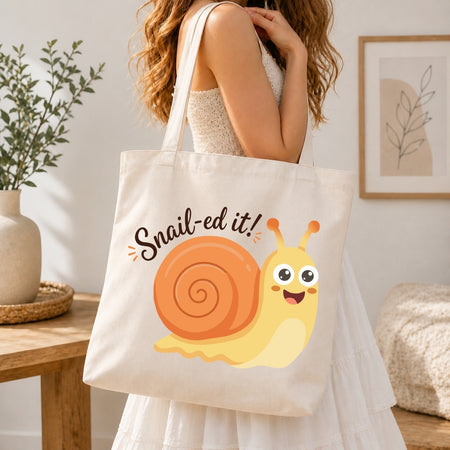 A person holding a cream-colored tote bag printed with the smiling cartoon snail graphic and the text "Snail-ed it!".