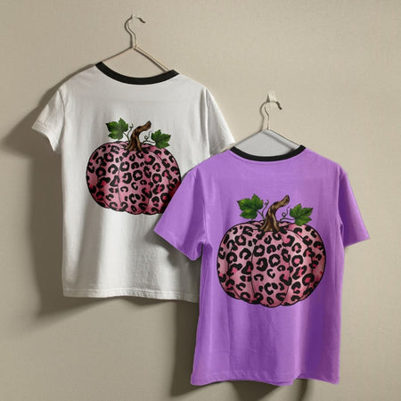 White and purple t-shirts with pink leopard print pumpkins on hangers against a beige wall.