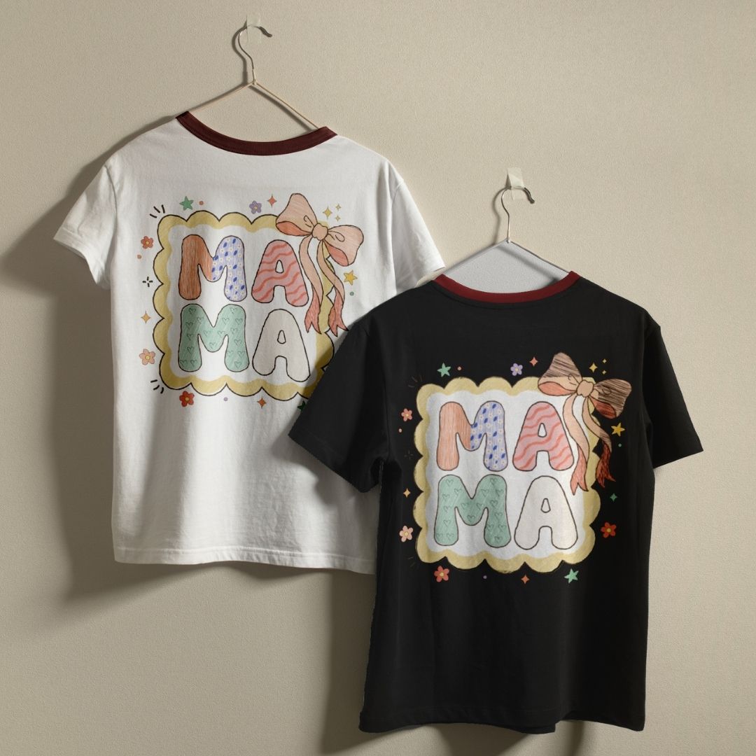 Two t-shirts, one white and one black, with 'MA MA' text and decorative elements on hangers against a beige background.