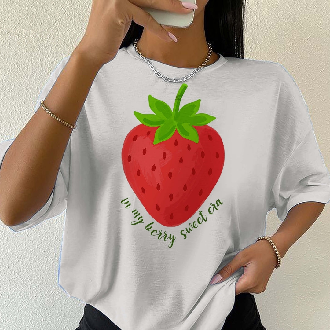 Person wearing a white t-shirt with a strawberry graphic and text.