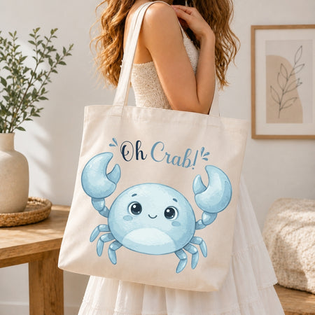 A woman holding a cream-colored tote bag printed with a blue cartoon crab graphic and the text "Oh Crab!"