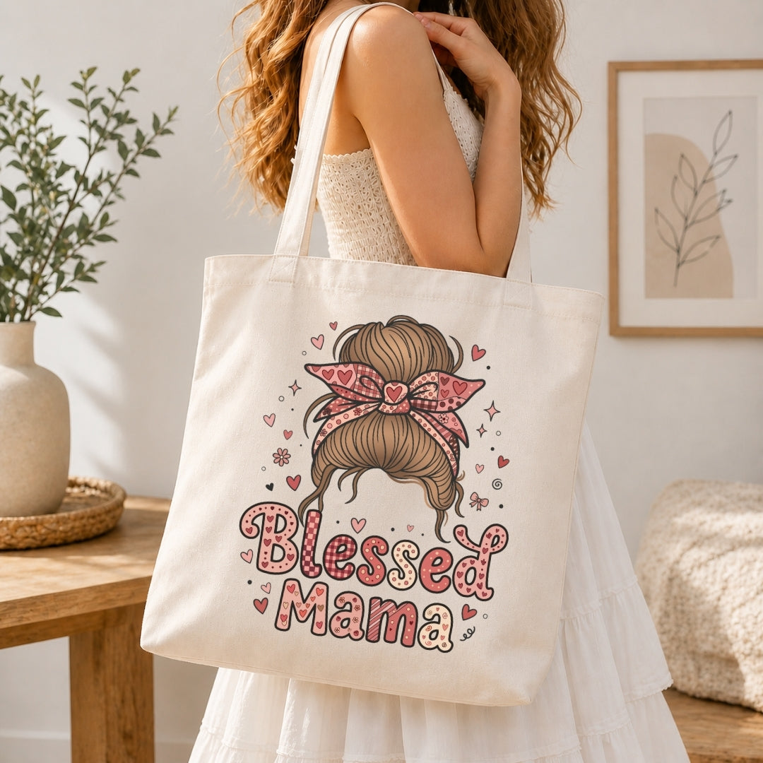 A woman in a white dress carries a cream canvas tote bag with a pink and brown graphic of a messy bun with a bow and the words 'Blessed Mama' in pink lettering, set in a bright, modern room.
