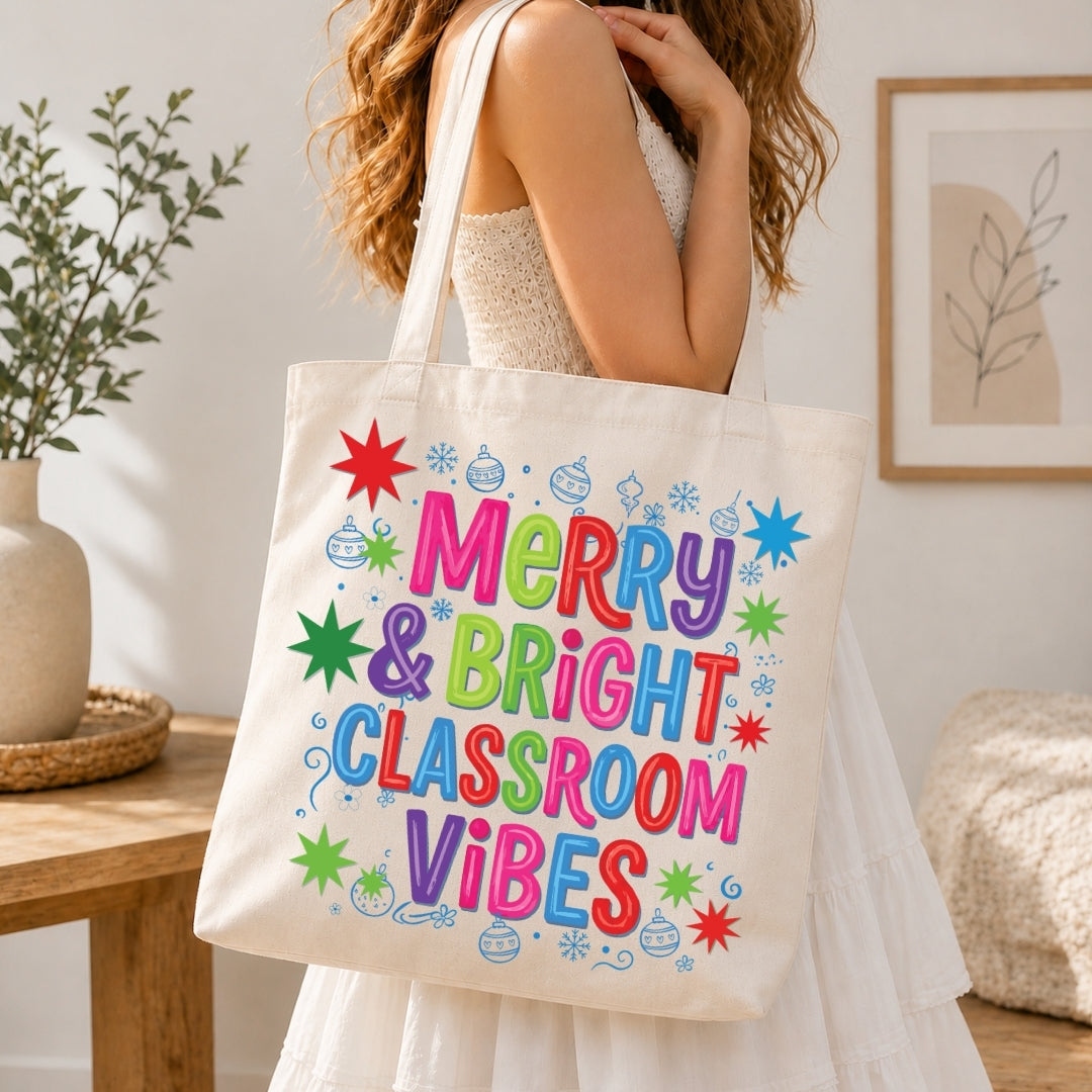 A woman in a white dress carries a cream canvas tote bag with colorful hand-lettered text reading 'Merry & Bright Classroom Vibes' surrounded by festive star and ornament illustrations, set in a bright, modern room.