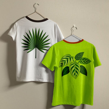 Two short-sleeve ringer T-shirts hanging on hangers against a plain beige wall. The left shirt is white with a dark brown collar and a large green palm leaf graphic on the back.