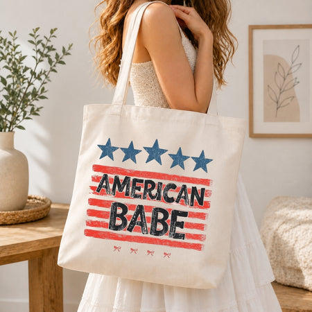 Person holding a tote bag with 'American Babe' design in a home setting