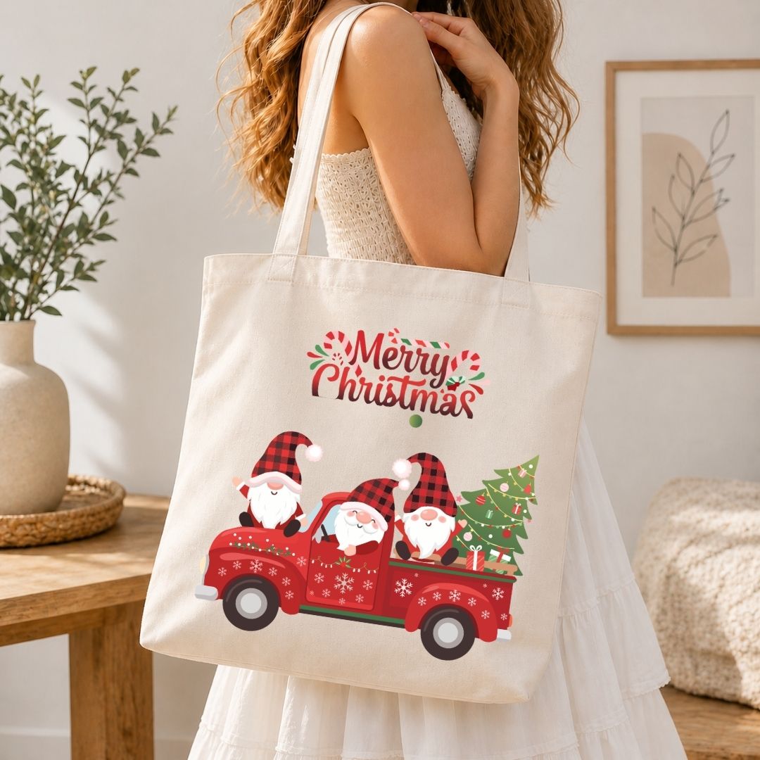 A woman in a white dress carries a cream canvas tote bag featuring a festive Christmas graphic of three Santa Claus figures in a red truck carrying a Christmas tree, with 'Merry Christmas' written above.