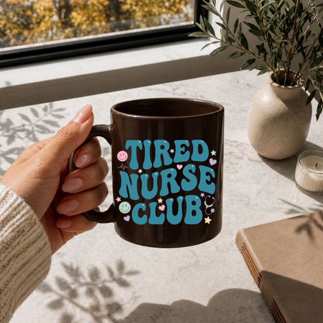 Hand holding a mug with 'Tired Nurse Club' text on a table with a window and plant in the background