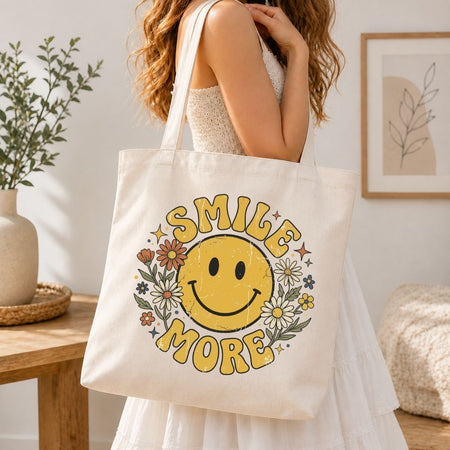 A woman carrying an over-the-shoulder cream canvas tote bag featuring a large vintage yellow smiley face illustration with flowers.