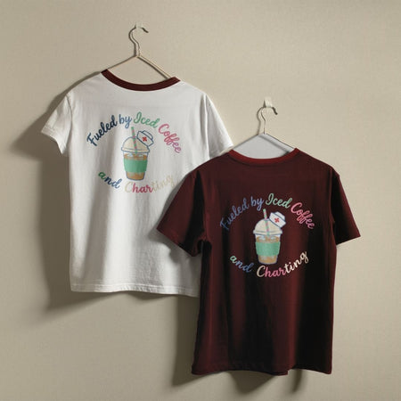Two t-shirts, one white and one maroon, with a graphic design and text on hangers against a beige wall.