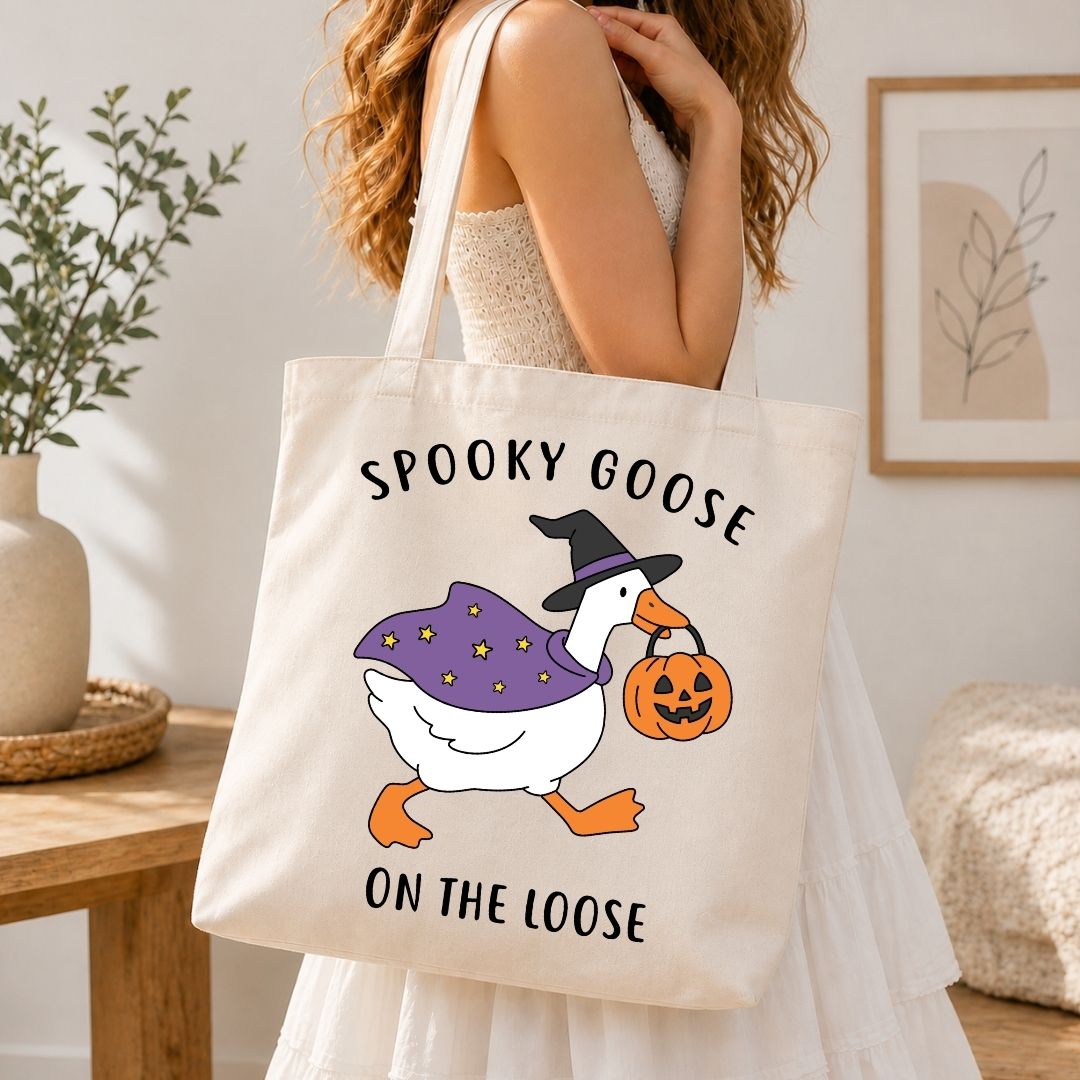 A person wearing a white dress and carrying a natural canvas tote bag printed with the Spooky Goose on the Loose Halloween design.