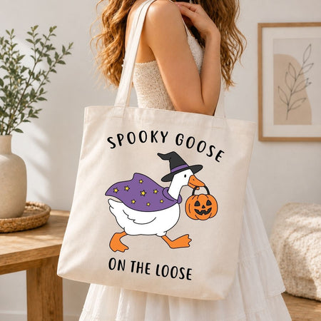A person wearing a white dress and carrying a natural canvas tote bag printed with the Spooky Goose on the Loose Halloween design.