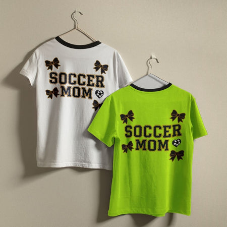 Two t-shirts with 'Soccer Mom' text on hangers against a beige background