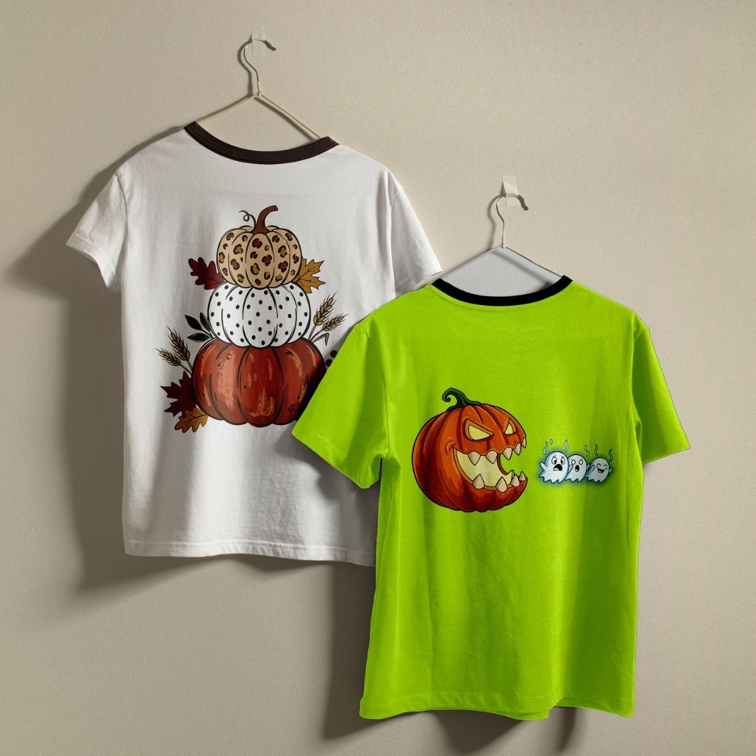 Two children's short-sleeve ringer T-shirts hanging on hangers against a plain beige wall. The left shirt is white with a dark brown collar and features a stacked autumn pumpkin design on the back.