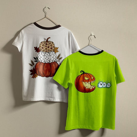 Two children's short-sleeve ringer T-shirts hanging on hangers against a plain beige wall. The left shirt is white with a dark brown collar and features a stacked autumn pumpkin design on the back.