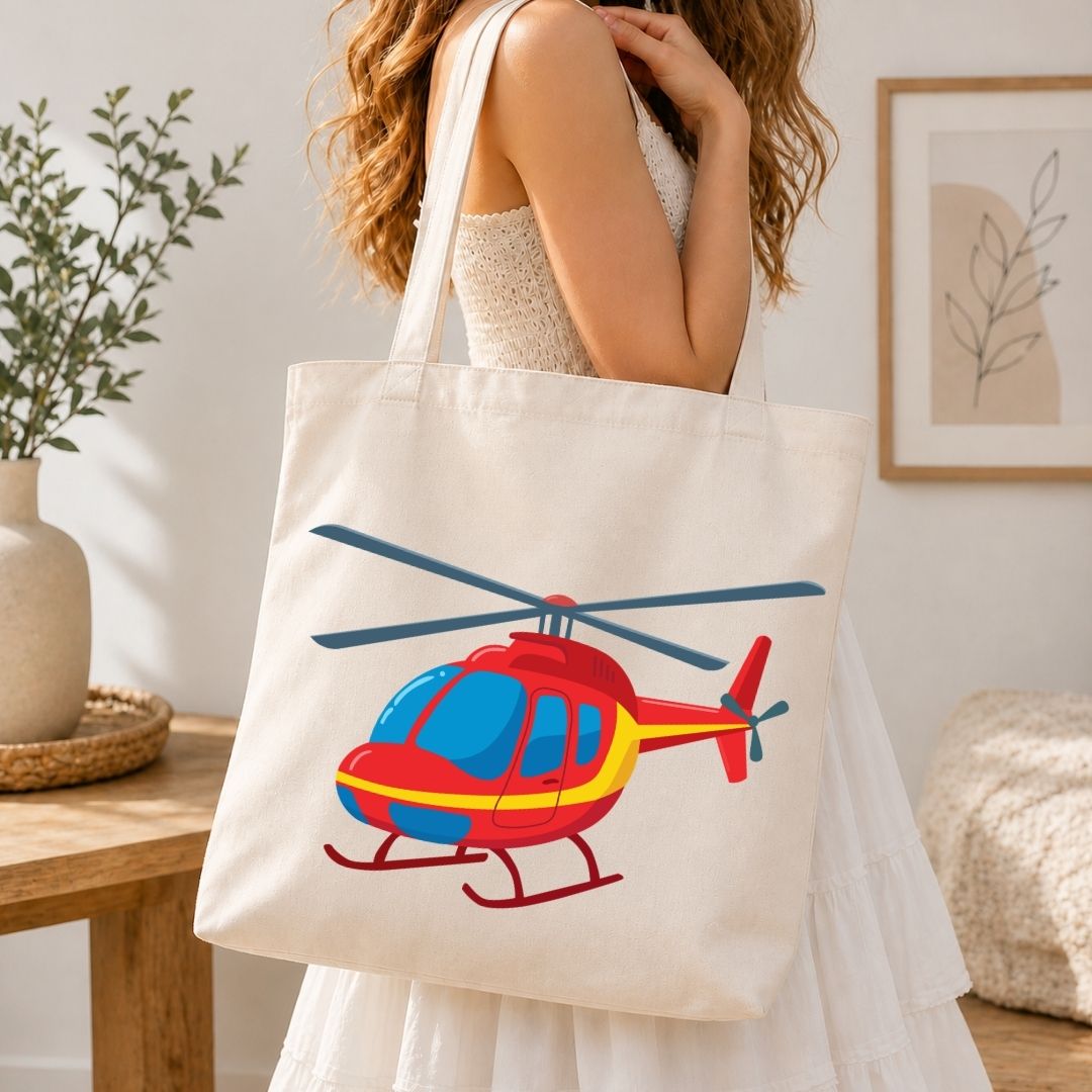 A woman wearing a white dress carries a cream canvas tote bag featuring a colorful cartoon helicopter graphic in red, yellow, and blue, set in a bright, modern room.