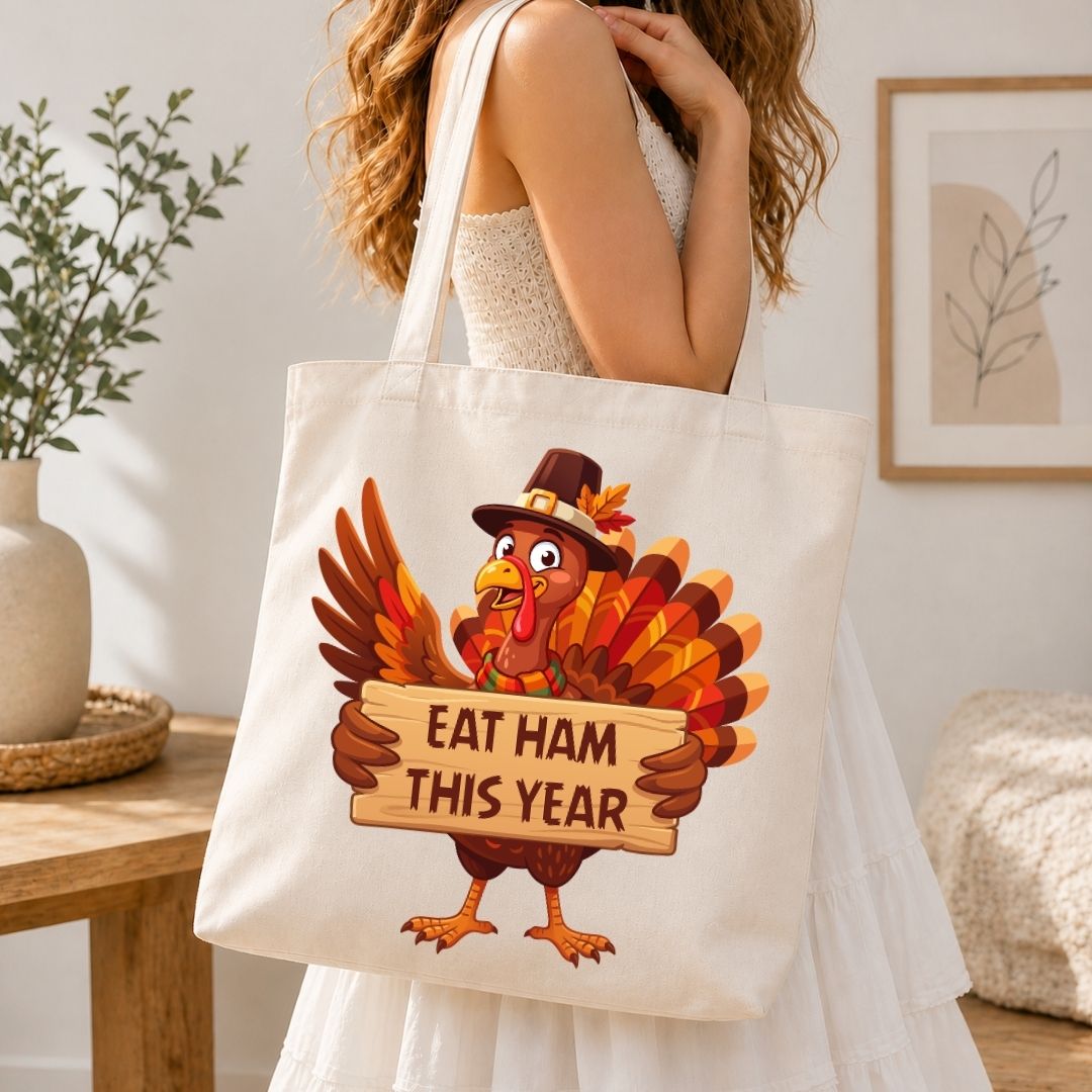 A woman wearing a white dress carries a cream canvas tote bag featuring a cartoon turkey holding a sign that reads 'EAT HAM THIS YEAR' in a cozy indoor setting.