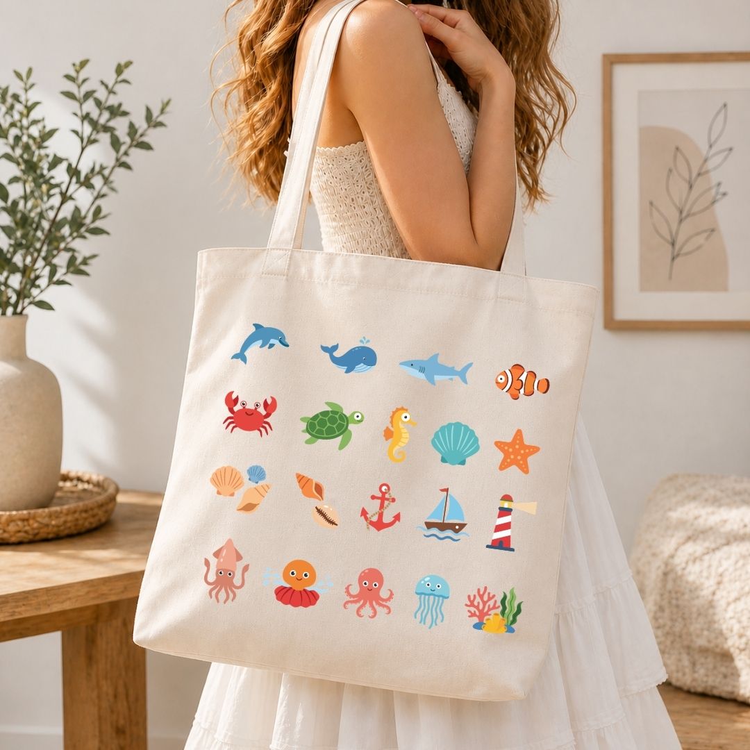 A woman in a white dress carries a cream canvas tote bag decorated with colorful ocean-themed illustrations including dolphins, a turtle, a crab, a seashell, and a lighthouse, set against a warm, softly lit indoor background.