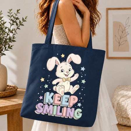 A woman over the shoulder carrying a dark blue canvas tote bag printed with a large, cute retro rabbit design and pastel letters spelling Keep Smiling.