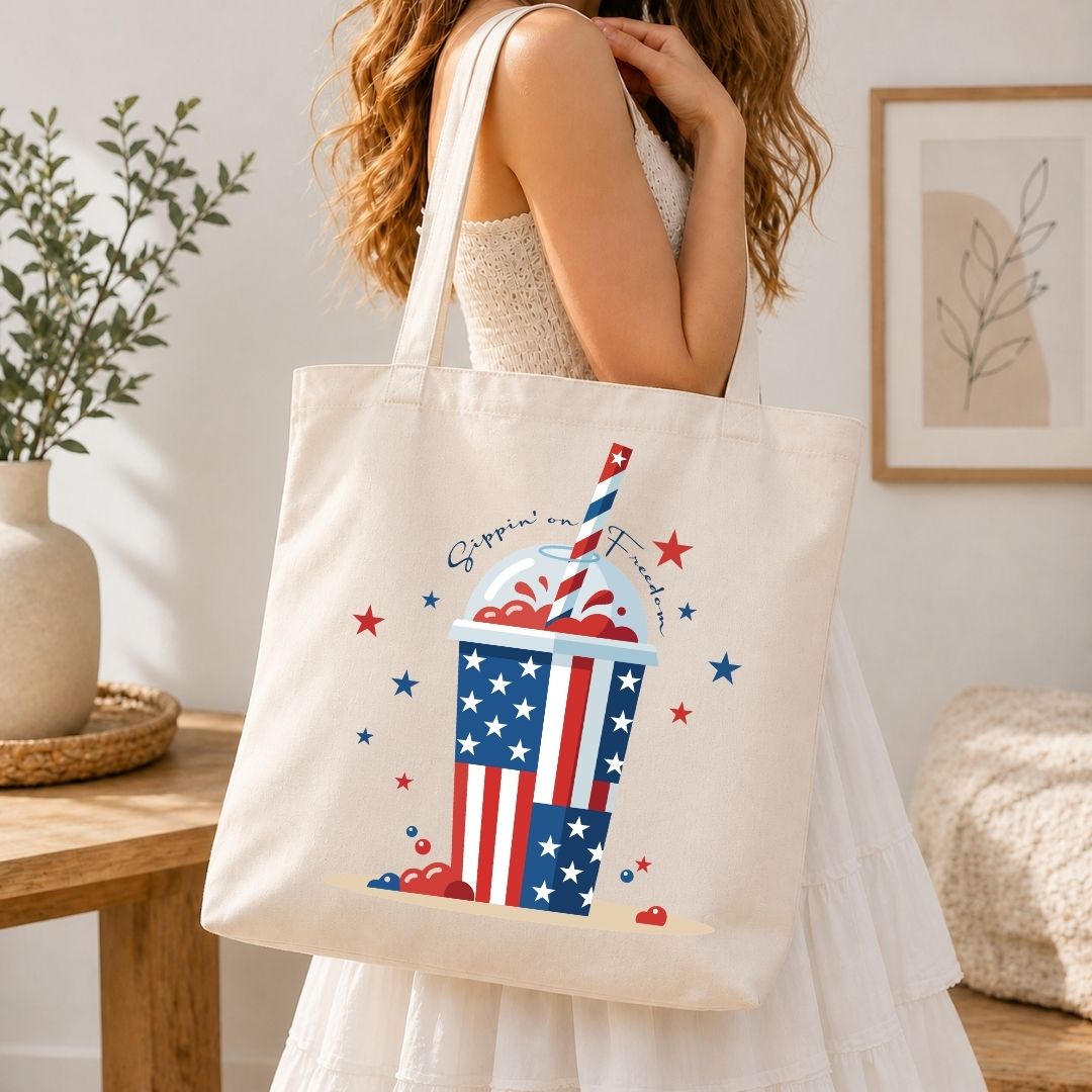 A woman carrying a cream-colored canvas tote bag over her shoulder printed with a large, vibrant 4th of July slushie cup design.