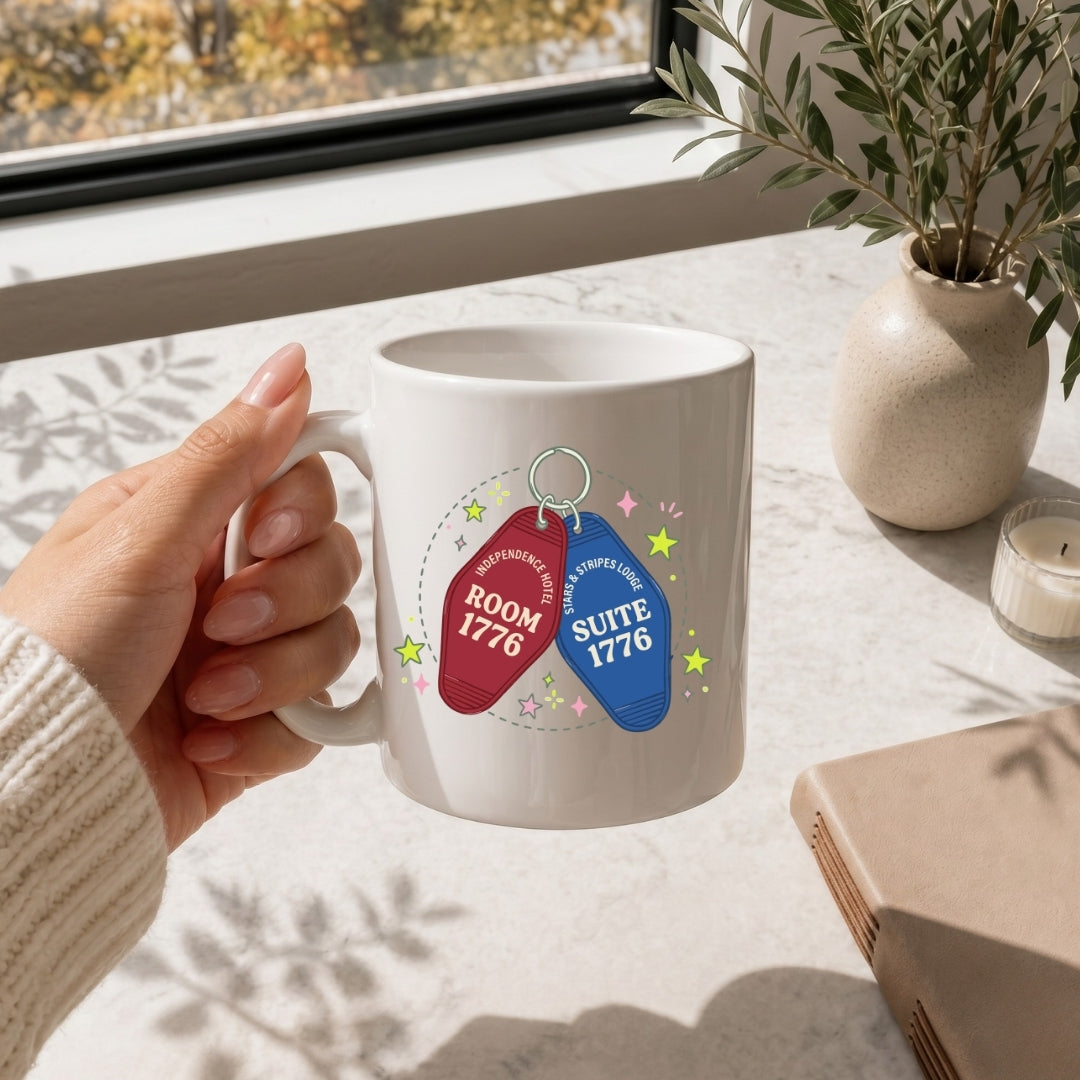 White mug with room and suite numbers held by a hand on a light surface with decor elements.