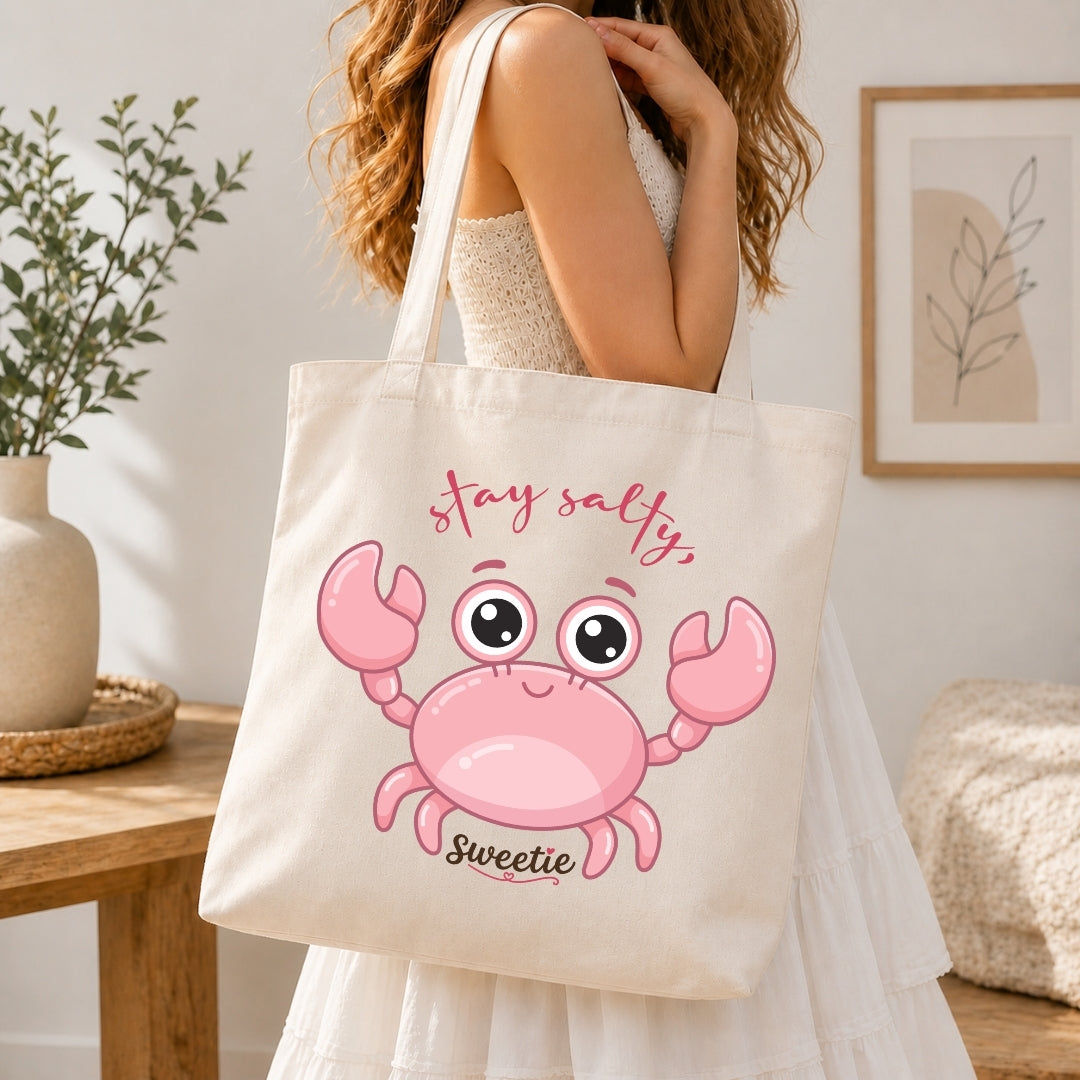 Person holding a tote bag with a pink crab design and text in a home setting