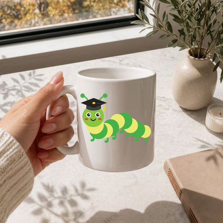 White mug with a caterpillar design holding a hand, placed on a light surface with a window and plant in the background.