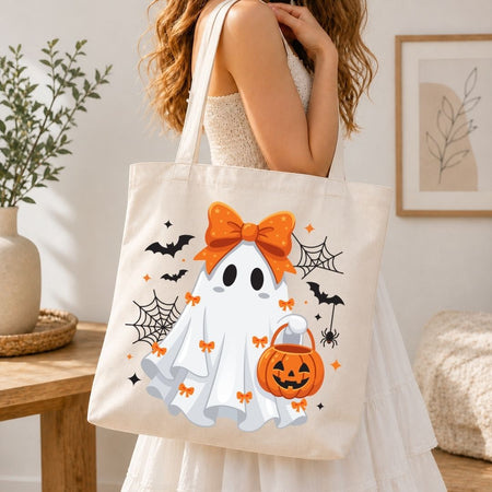 Woman holding a canvas tote bag printed with a cute Halloween ghost and pumpkin bucket design.