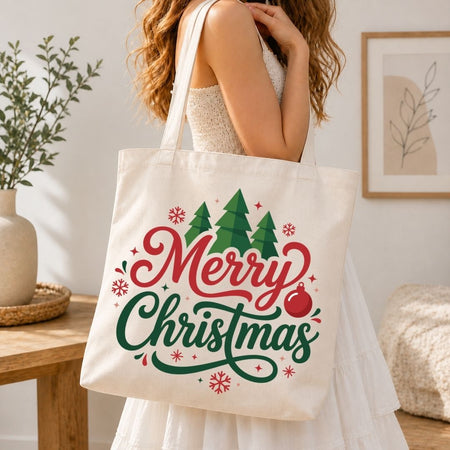 Woman holding a canvas tote bag printed with a "Merry Christmas" typography, pine trees, and snowflake holiday design.