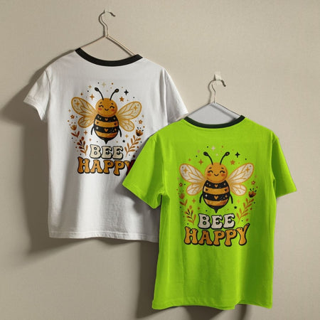 Two t-shirts, one white and one green, with a bee design and 'BEE HAPPY' text on hangers against a beige background.