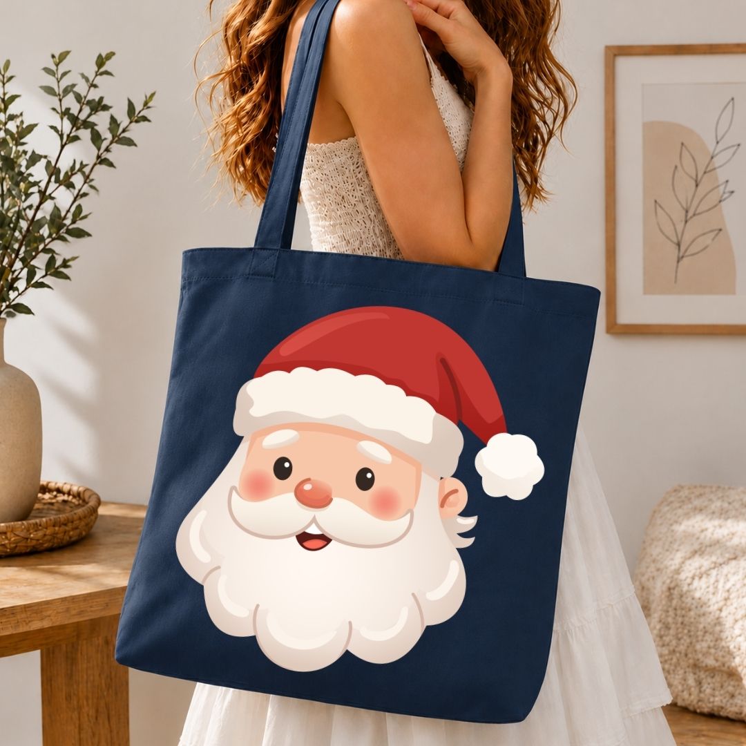 A navy blue canvas tote bag with a large cartoon Santa Claus face graphic, carried by a woman in a white dress in a cozy indoor setting.