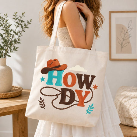 A woman carrying a cream-colored canvas tote bag over her shoulder printed with a large, vibrant Western "Howdy" design with a lasso rope.