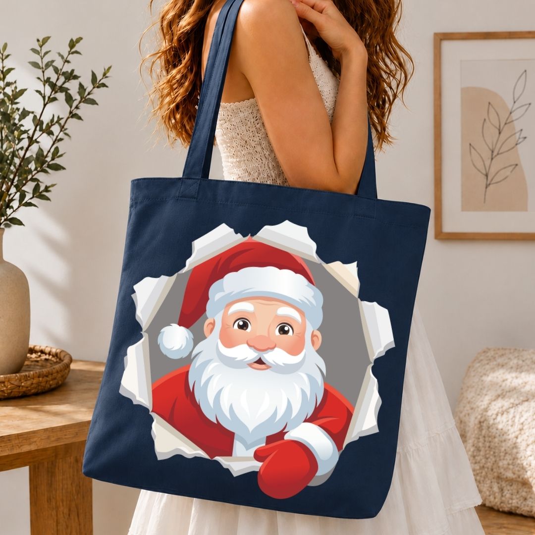 Woman holding a navy blue canvas tote bag printed with a cartoon Santa Claus bursting through a torn paper graphic.