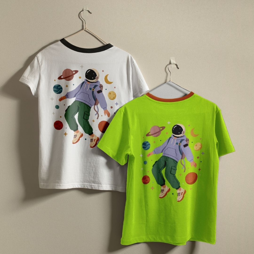 Two t-shirts, one white and one green, with a space-themed design of an astronaut on hangers against a beige wall.